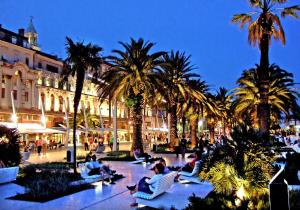 a group of people sitting in chairs in a courtyard with palm trees at Apartment heart of the city in Split