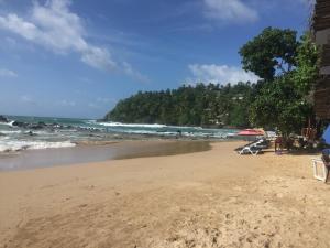 una playa con sillas y sombrilla y el océano en Margosa Guesthouse, en Mirissa