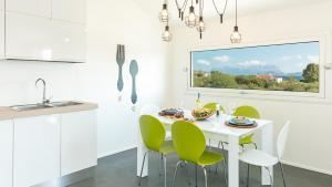 a white kitchen with a white table and green chairs at Sardegna é - Villa Charme&Design in Olbia