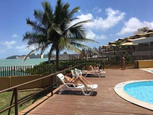 2 personas sentadas en sillones junto a una piscina en Atlântico Flat 110, en Natal