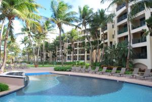 a pool with chairs and palm trees in front of a building at 1 bedroom beachfront Apartment at Rio Mar in Rio Grande