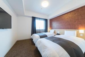 a hotel room with two beds and a television at Dormy Inn Matsuyama Natural Hot Spring in Matsuyama