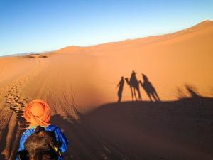 a group of people walking in the desert with their shadows at Nomadic Desert Camp Tours in Merzouga