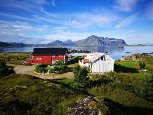 a red and white barn on a field with a body of water at Lofoten Ocean View - Sandøy Gård in Sand