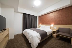 a hotel room with a bed and a chair at Dormy Inn Matsuyama Natural Hot Spring in Matsuyama