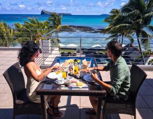 un hombre y una mujer sentados en una mesa comiendo comida en Cape Point Seafront Suites & Penthouse by LOV en Cap Malheureux