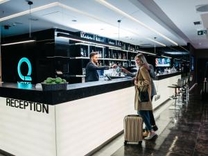 a woman with a suitcase standing in front of a bar at Q Hotel Plus Kraków in Kraków