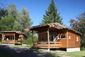 eine große Holzhütte mit einer Veranda in einem Wald in der Unterkunft Camping Les Vernieres La Bourboule Sancy in La Bourboule
