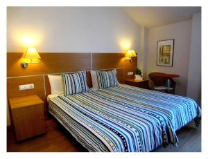 a bedroom with a bed with a striped comforter and two lamps at Hotel Rural Latxanea in Alsasua