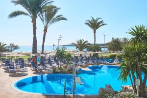 a pool with chairs and palm trees and the ocean at Hipotels Hipocampo Playa in Cala Millor