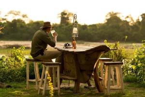 a man sitting at a table with a bottle of beer at Selous River Camp in Kwangwazi