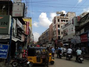 uma rua movimentada da cidade com pessoas em motocicletas e carros em Mani's residency em Madurai