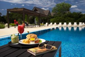 a table with a sandwich and a drink next to a pool at Real Colonia Hotel & Suites in Colonia del Sacramento