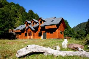 a large wooden house in a field with a log at Refugio Las Raices in Malalcahuello