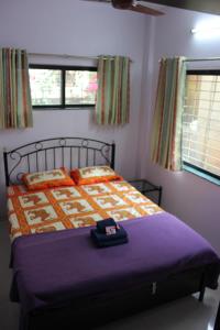 a bedroom with a bed with a purple blanket and two windows at Om Bungalow -Happy Stay At Panchgani in Panchgani