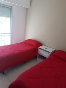 two beds in a room with red sheets and a table at Frente al Río in Paraná