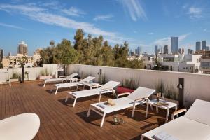 um pátio com cadeiras brancas e mesas num telhado em Shenkin Hotel em Tel Aviv