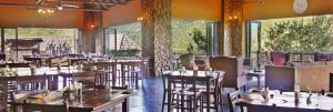 um restaurante com mesas e cadeiras de madeira e janelas grandes em Mabalingwe Elephant Lodge em Bela-Bela