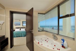 a bathroom with a bath tub and a bedroom at Beach Hotel Swakopmund in Swakopmund