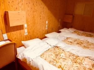 two unmade beds in a room with wooden walls at Guesthouse Otaru Wanokaze in Otaru