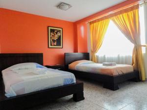 two beds in a room with orange walls and a window at Hostal La Rosa Otavalo in Otavalo