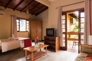 a room with a bed and a tv and a table at Pousada Ilhote da Prainha in Ilhabela