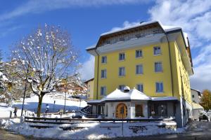 a yellow building with snow on the ground at Hotel Vittoria in Folgaria