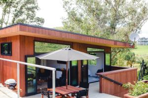 a house with a deck with an umbrella and a table at Amongst The Nikau in Waihi Beach