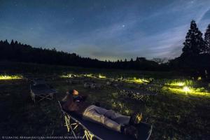南阿蘇村的住宿－南阿蘇月神天文台/森林畫室旅館，夜间躺在田野的长椅上的人