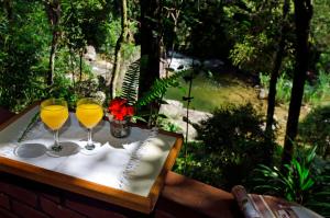 two wine glasses on a table with a view of a river at Pousada do Rio Maua in Visconde De Maua