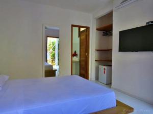 1 dormitorio con 1 cama blanca y TV de pantalla plana en Hospedaria Zukka Trancoso, en Trancoso
