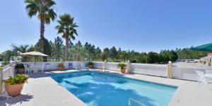 a swimming pool with chairs and a fence and palm trees at Americas Best Value Inn Hazlehurst in Hazlehurst