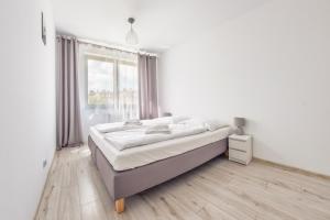 a white bedroom with a large bed and a window at Apartamenty Sun & Snow Kwartał Róży Wiatrów in Świnoujście