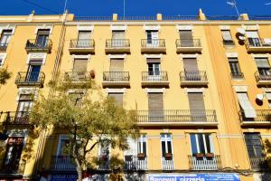Hola Valencia - Holiday Apartments في فالنسيا: مبنى اصفر وامامه بلكونات واشجار