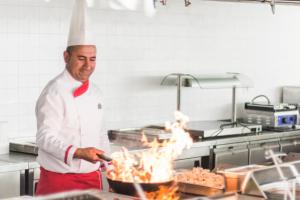 a chef cooking food in a kitchen with flames at Laguna Beach Alya Resort & Spa in Okurcalar