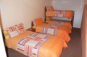 three beds in a room with orange sheets at Hotel Residencial El Viajero in Tababela