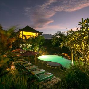 a pool with chairs and umbrellas in front of a building at Uma Agung Villa in Sidemen