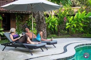 um homem e uma mulher sentados em cadeiras de jardim debaixo de um guarda-sol junto a uma piscina em Pearl Boutique Hotel Adult only em Legian