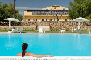 una mujer sentada en el borde de una piscina en Hotel Villa Calandrino, en Sciacca