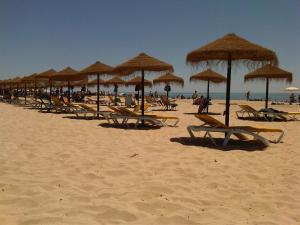 un grupo de sillas de playa y sombrillas en una playa en Casa da Madrinha II en Monte Gordo