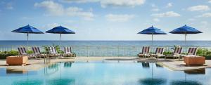 a swimming pool with chairs and umbrellas and the ocean at Eau Palm Beach Resort & Spa in Palm Beach