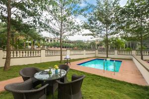 Un patio con mesa y sillas y una piscina. en StayVista's Greenwoods Villa 7 - City-Center Villa with Private Pool, Terrace, Lift & Ping-Pong Table, en Lonavala