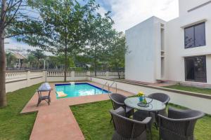Un patio con mesa y sillas y una piscina. en StayVista's Greenwoods Villa 7 - City-Center Villa with Private Pool, Terrace, Lift & Ping-Pong Table, en Lonavala