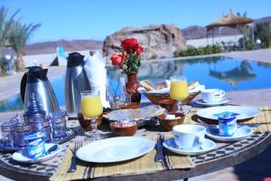 a table with plates of food and drinks next to a pool at Dar Alfourssane Ferme d’hôte in Ouarzazate