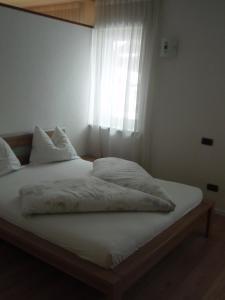 Bett mit weißer Bettwäsche und Kissen vor einem Fenster in der Unterkunft Klaus Luttach in Luttach