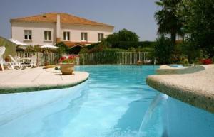 une grande piscine bleue avec une maison en arrière-plan dans l'établissement Atlantis Hôtel, à Mimizan