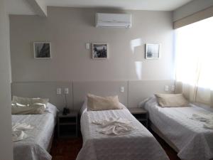 um quarto com três camas com lençóis brancos em Botucatu Hotel em Botucatu