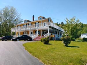 a large yellow house with cars parked in the driveway at The Island Inn in Ingonish Beach