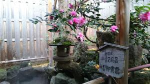 un jardín con un baño de aves y flores rosas en Onyado Hishiya Torazo, en Yamanouchi
