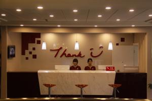 dos personas sentadas en un mostrador con una señal de agradecimiento en Thank Inn Chain Hotel Huebei Jinmen Jingshan County Chengzhong Road en Jingshan